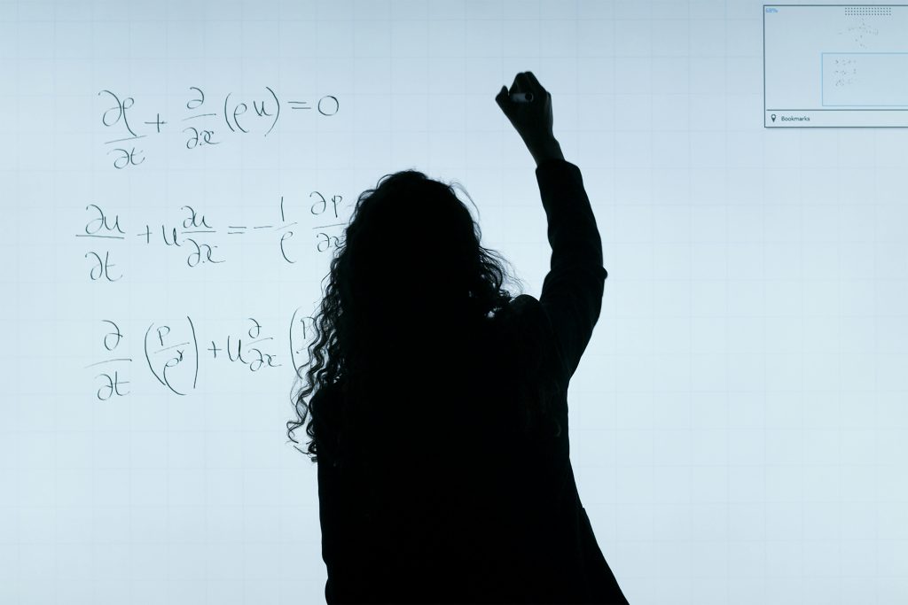 A silhouette of a woman writing mathematical equations on a large whiteboard, representing education and analysis.